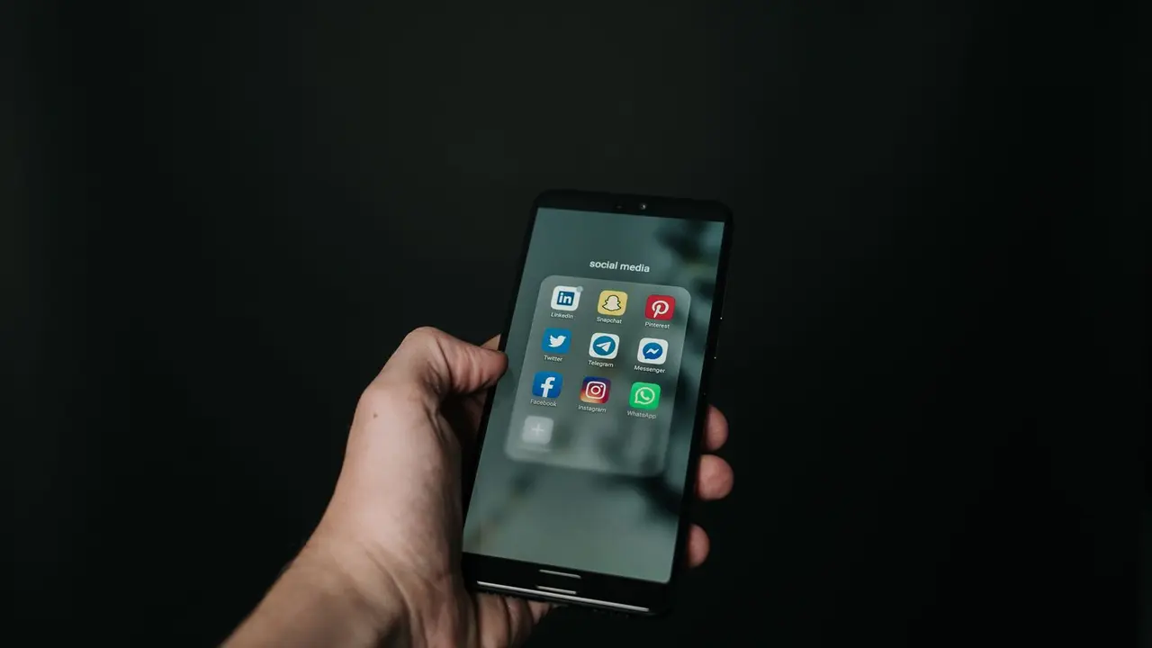 Hand hält ein Smartphone mit App-Symbolen vor dunklem Hintergrund