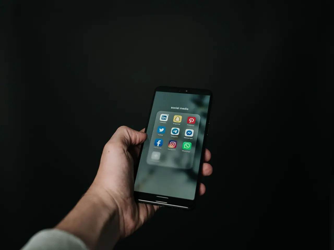 Hand hält ein Smartphone mit App-Symbolen vor dunklem Hintergrund