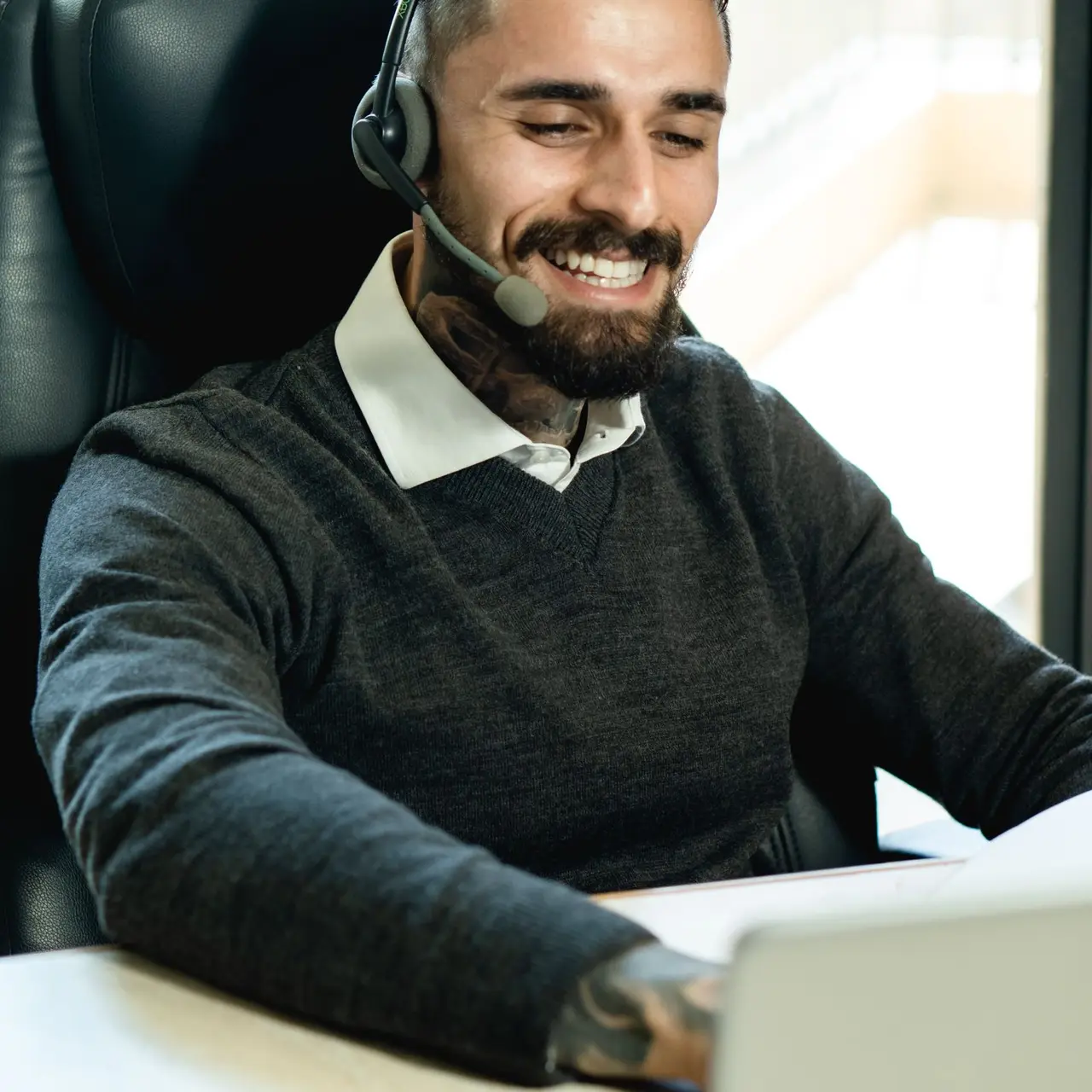 Lächelnder Mitarbeiter mit Headset am Laptop